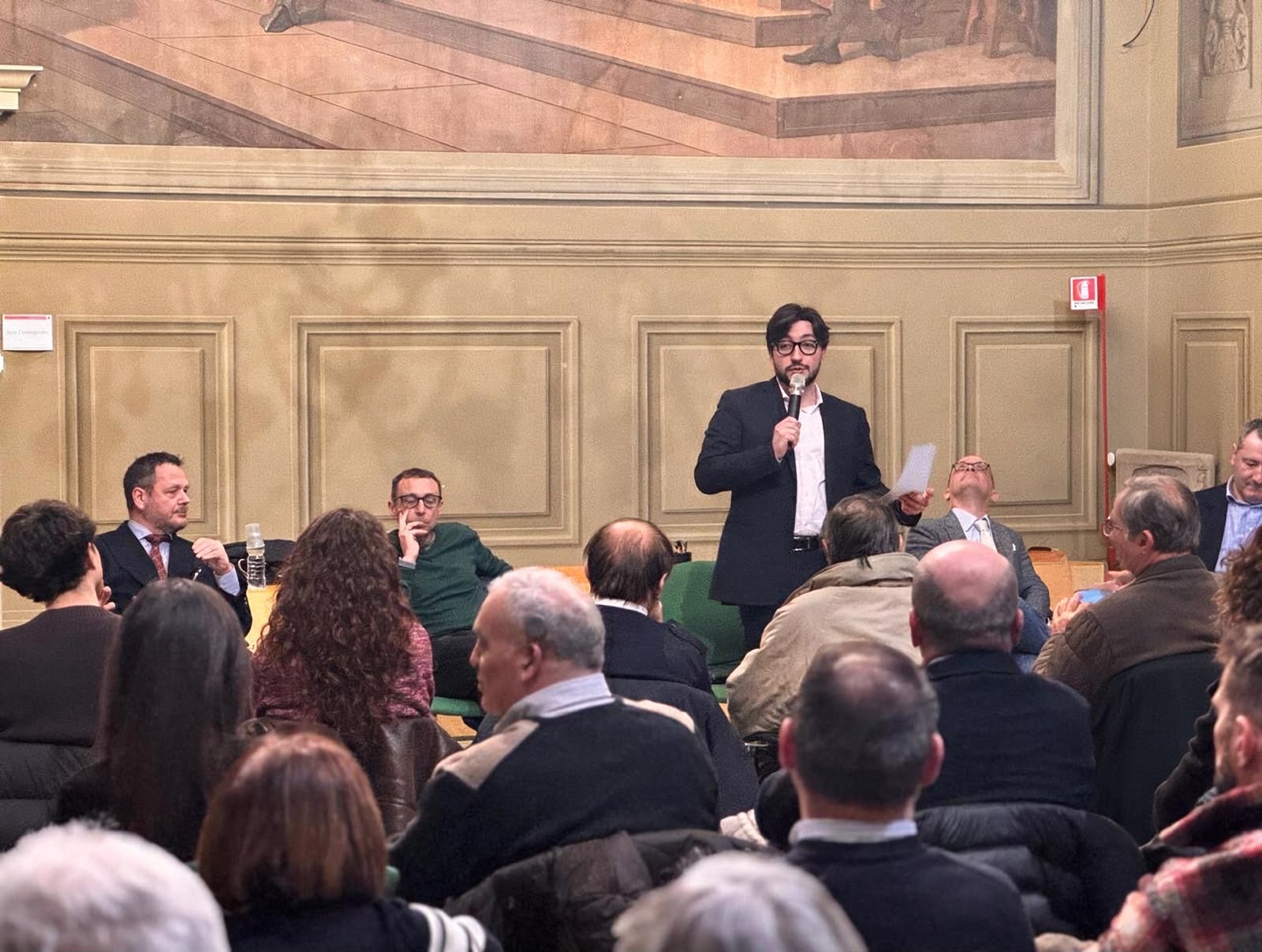 Leonardo Gallozzi parla al microfono davanti a una sala piena durante un incontro pubblico