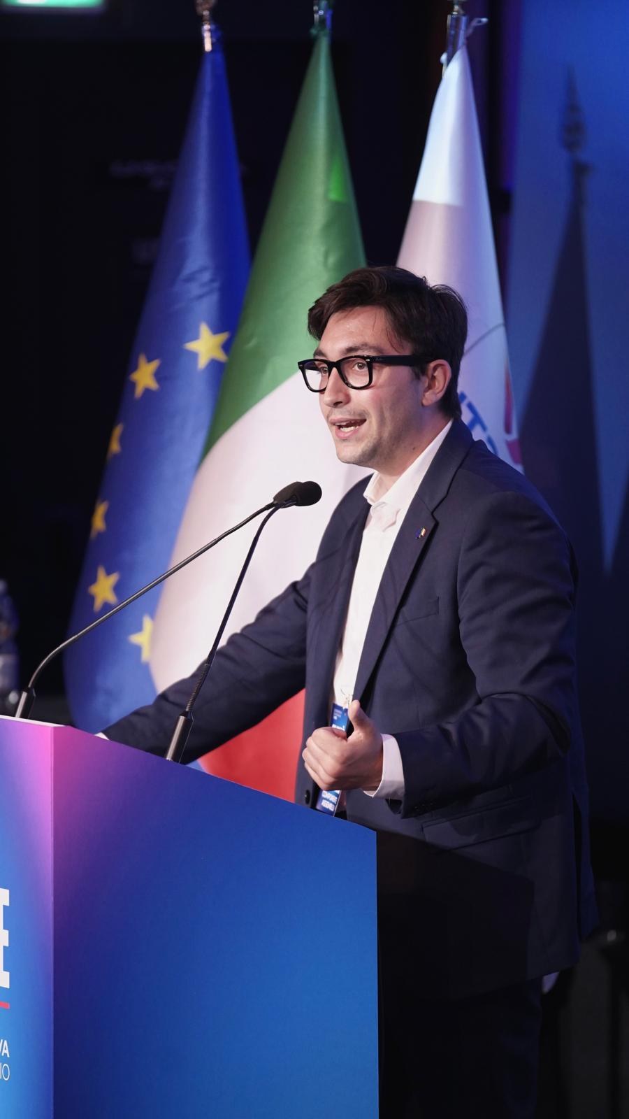 Leonardo Gallozzi parla dal palco davanti alle bandiere italiana ed europea